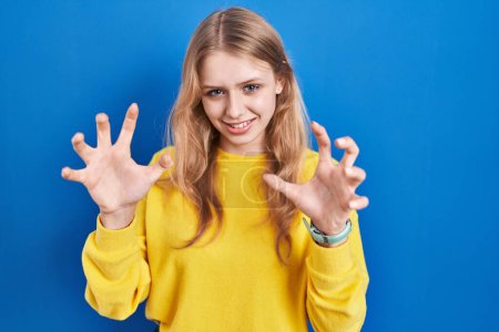 Photo for Young caucasian woman standing over blue background smiling funny doing claw gesture as cat, aggressive and sexy expression - Royalty Free Image