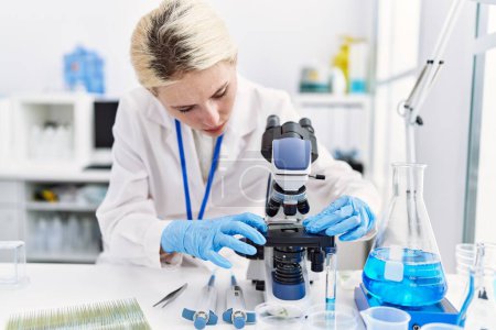 Téléchargez les photos : Jeune femme blonde scientifique utilisant un microscope souriant au laboratoire - en image libre de droit