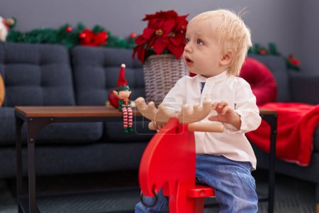 Photo for Adorable blond toddler playing with reindeer rocking by christmas decoration at home - Royalty Free Image