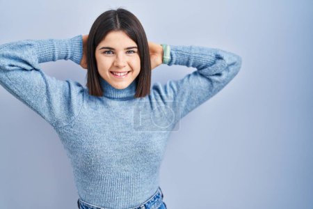 Téléchargez les photos : Jeune femme hispanique debout sur fond bleu relaxant et étirant, bras et mains derrière la tête et le cou souriant heureux - en image libre de droit