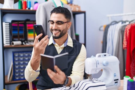 Téléchargez les photos : Jeune homme arabe tailleur parler sur le portable de lecture smartphone à l'usine de vêtements - en image libre de droit
