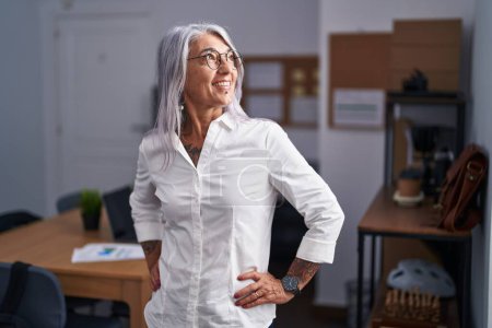 Téléchargez les photos : Femme d'âge moyen aux cheveux gris travailleur d'affaires souriant confiant debout au bureau - en image libre de droit