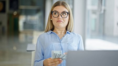 Téléchargez les photos : Jeune femme blonde travailleur d'affaires en utilisant des dollars de comptage d'ordinateur portable au bureau - en image libre de droit