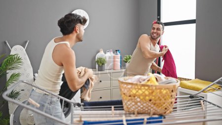 Photo for Two men doing laundry throwing clothes at laundry room - Royalty Free Image