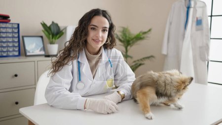 Foto de Mujer hispana joven con veterinario perro sonriendo confiado en la clínica - Imagen libre de derechos