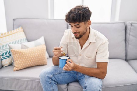 Photo for Young arab man pouring liquid on coffee sitting on sofa at home - Royalty Free Image