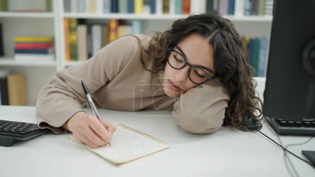 Foto de Joven mujer hispana hermosa estudiante escribiendo notas cansadas en la universidad de la biblioteca - Imagen libre de derechos