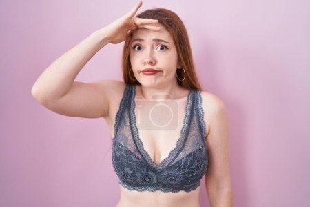 Photo for Redhead woman wearing lingerie over pink background worried and stressed about a problem with hand on forehead, nervous and anxious for crisis - Royalty Free Image