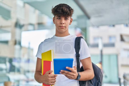 Téléchargez les photos : Jeune adolescent hispanique étudiant utilisant touchpad tenant des livres à l'université - en image libre de droit