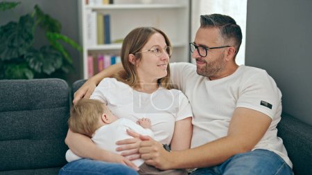 Photo for Family of mother, father and baby breastfeeding sitting on the sofa at home - Royalty Free Image