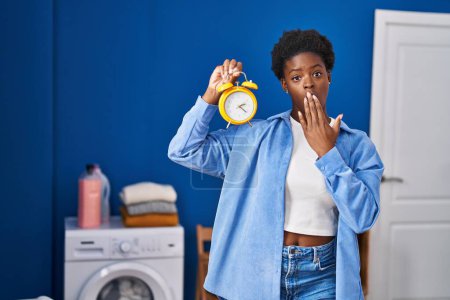 Téléchargez les photos : Femme afro-américaine attendant la lessive couvrant la bouche avec la main, choquée et effrayée par l'erreur. expression surprise - en image libre de droit