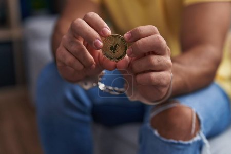 Téléchargez les photos : Jeune homme hispanique criminel tenant uniswap crypto monnaie portant des menottes à la maison - en image libre de droit