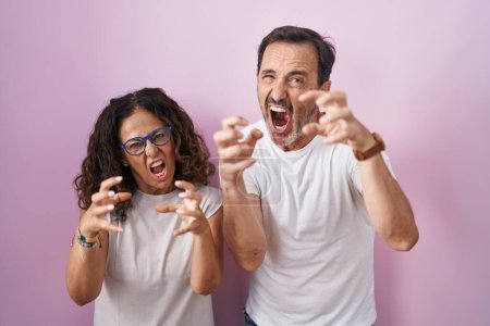 Téléchargez les photos : Couple hispanique du Moyen Âge ensemble sur fond rose criant frustré par la rage, mains essayant d'étrangler, hurlant fou - en image libre de droit