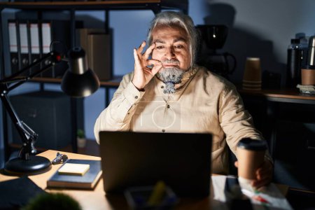 Foto de Hombre de mediana edad con el pelo gris trabajando en la oficina por la noche boca y los labios cerrados como cremallera con los dedos. secreto y silencioso, tabú hablando - Imagen libre de derechos