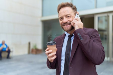 Téléchargez les photos : Moyen âge homme d'affaires travailleur parlant sur smartphone boire du café dans la rue - en image libre de droit