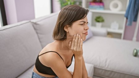 Téléchargez les photos : Jeune belle femme hispanique assise sur un canapé souffrant de maux de dents à la maison - en image libre de droit