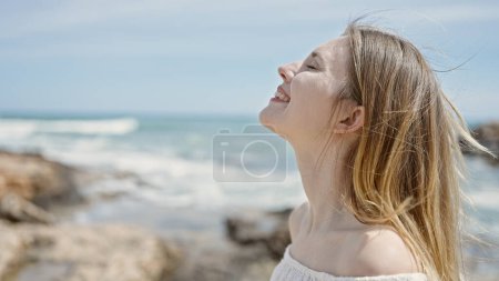 Foto de Joven mujer rubia turista sonriendo confiado respirando en la playa - Imagen libre de derechos