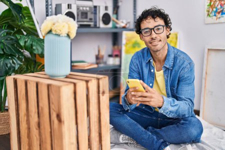 Photo for Young hispanic man artist smiling confident using smartphone at art studio - Royalty Free Image