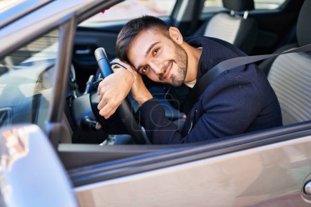 Foto de Joven hombre hispano sonriendo confiado apoyado en el volante en la calle - Imagen libre de derechos