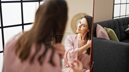 Photo for Young beautiful hispanic woman combing hair looking herself on mirror at home - Royalty Free Image