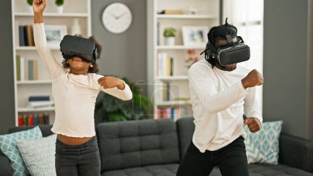 Téléchargez les photos : African American père et fille jouer à un jeu vidéo en utilisant des lunettes de réalité virtuelle à la maison - en image libre de droit