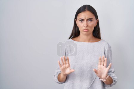 Photo for Young hispanic woman standing over white background moving away hands palms showing refusal and denial with afraid and disgusting expression. stop and forbidden. - Royalty Free Image
