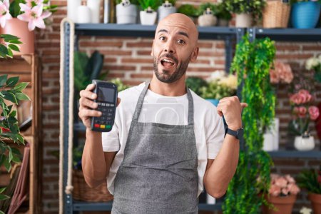 Photo for Middle age bald man working at florist shop holding dataphone pointing thumb up to the side smiling happy with open mouth - Royalty Free Image