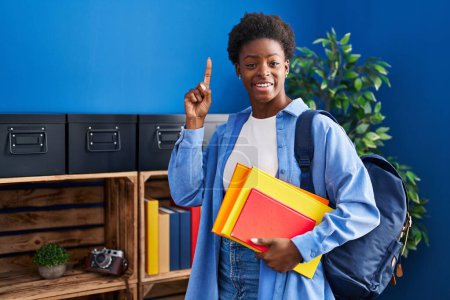 Photo for African american woman wearing student backpack and holding books surprised with an idea or question pointing finger with happy face, number one - Royalty Free Image