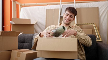 Photo for Young hispanic man smiling confident unpacking cardboard box at new home - Royalty Free Image
