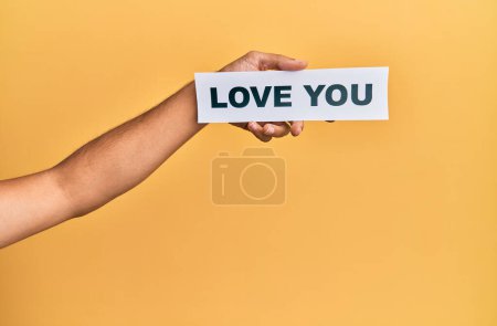 Foto de Mano de hombre caucásico sosteniendo papel con amor mensaje sobre fondo amarillo aislado - Imagen libre de derechos