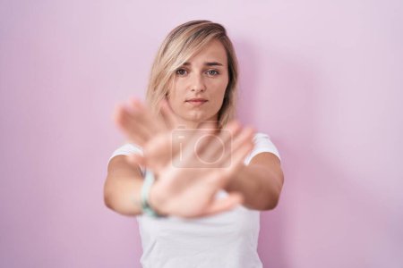 Téléchargez les photos : Jeune femme blonde debout sur fond rose expression de rejet croisement des bras et des paumes faisant signe négatif, visage en colère - en image libre de droit