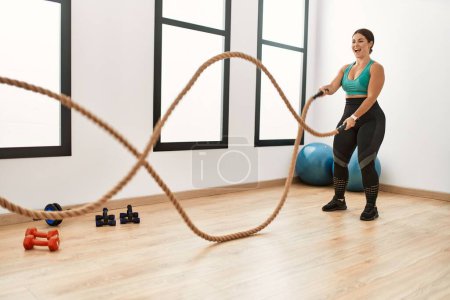Photo for Young beautiful hispanic woman smiling confident using battle rope training at sport center - Royalty Free Image