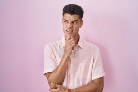 Photo for Young hispanic man standing over pink background thinking worried about a question, concerned and nervous with hand on chin - Royalty Free Image