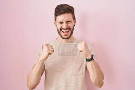 Foto de Hombre hispano con barba de pie sobre fondo rosa emocionado por el éxito con los brazos levantados y los ojos cerrados celebrando la victoria sonriendo. concepto ganador. - Imagen libre de derechos