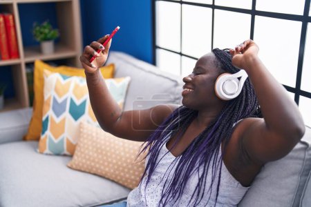 Photo for African american woman dancing and listening to music sitting on sofa at home - Royalty Free Image