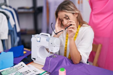 Foto de Joven mujer rubia sastre estresado usando máquina de coser en tienda de ropa - Imagen libre de derechos