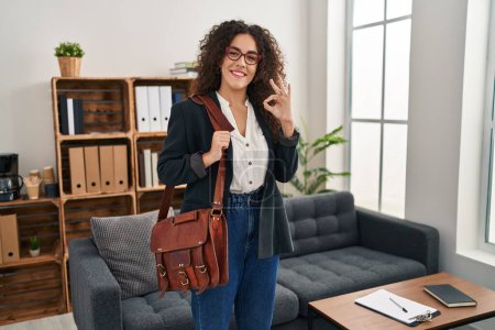 Photo for Young hispanic woman at consultation office doing ok sign with fingers, smiling friendly gesturing excellent symbol - Royalty Free Image