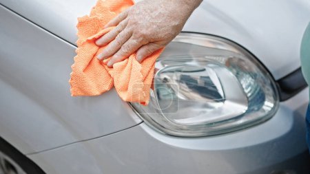 Photo for Middle age grey-haired man cleaning car headlights at street - Royalty Free Image