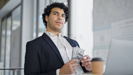 Téléchargez les photos : Young latin man business worker using laptop counting dollars at office - en image libre de droit