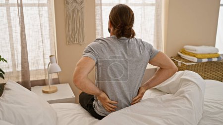 Téléchargez les photos : Young hispanic man suffering for backache sitting on bed at bedroom - en image libre de droit