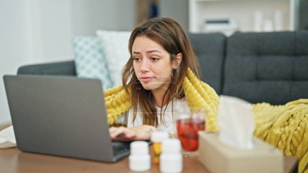 Téléchargez les photos : Jeune belle femme hispanique assise sur le sol malade ayant une consultation médicale en ligne sur ordinateur portable à la maison - en image libre de droit