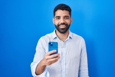 Téléchargez les photos : Homme hispanique avec barbe en utilisant un message de dactylographie smartphone avec un sourire heureux et cool sur le visage. chanceux. - en image libre de droit