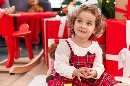 Photo for Adorable hispanic toddler sitting on floor by christmas gifts at home - Royalty Free Image