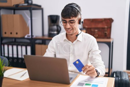 Foto de Joven hombre hispano que trabaja usando computadora portátil con tarjeta de crédito con una sonrisa alegre y fresca en la cara. persona afortunada. - Imagen libre de derechos
