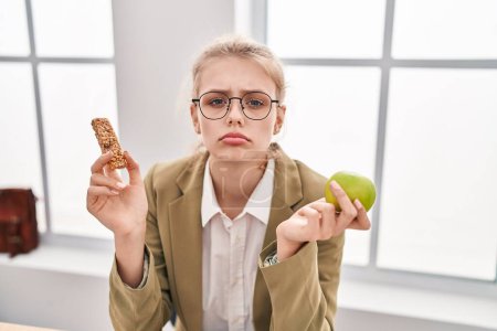 Photo for Young caucasian woman working at the office eating snack depressed and worry for distress, crying angry and afraid. sad expression. - Royalty Free Image