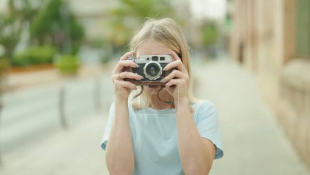 Foto de Young blonde woman tourist using vintage camera at street - Imagen libre de derechos