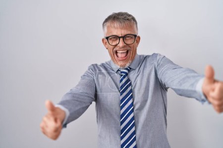 Foto de Hombre de negocios hispano con el pelo gris usando gafas aprobando hacer gesto positivo con la mano, pulgares arriba sonriendo y feliz por el éxito. gesto ganador. - Imagen libre de derechos