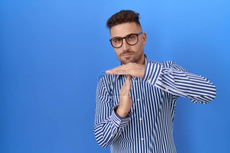 Photo for Hispanic man with beard wearing glasses doing time out gesture with hands, frustrated and serious face - Royalty Free Image