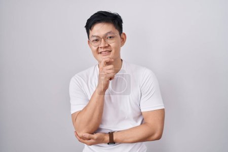 Photo for Young asian man standing over white background with hand on chin thinking about question, pensive expression. smiling and thoughtful face. doubt concept. - Royalty Free Image