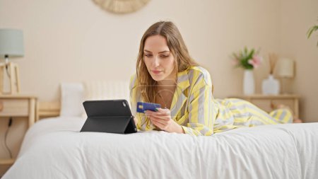 Photo for Young blonde woman shopping with touchpad and credit card lying on bed at bedroom - Royalty Free Image